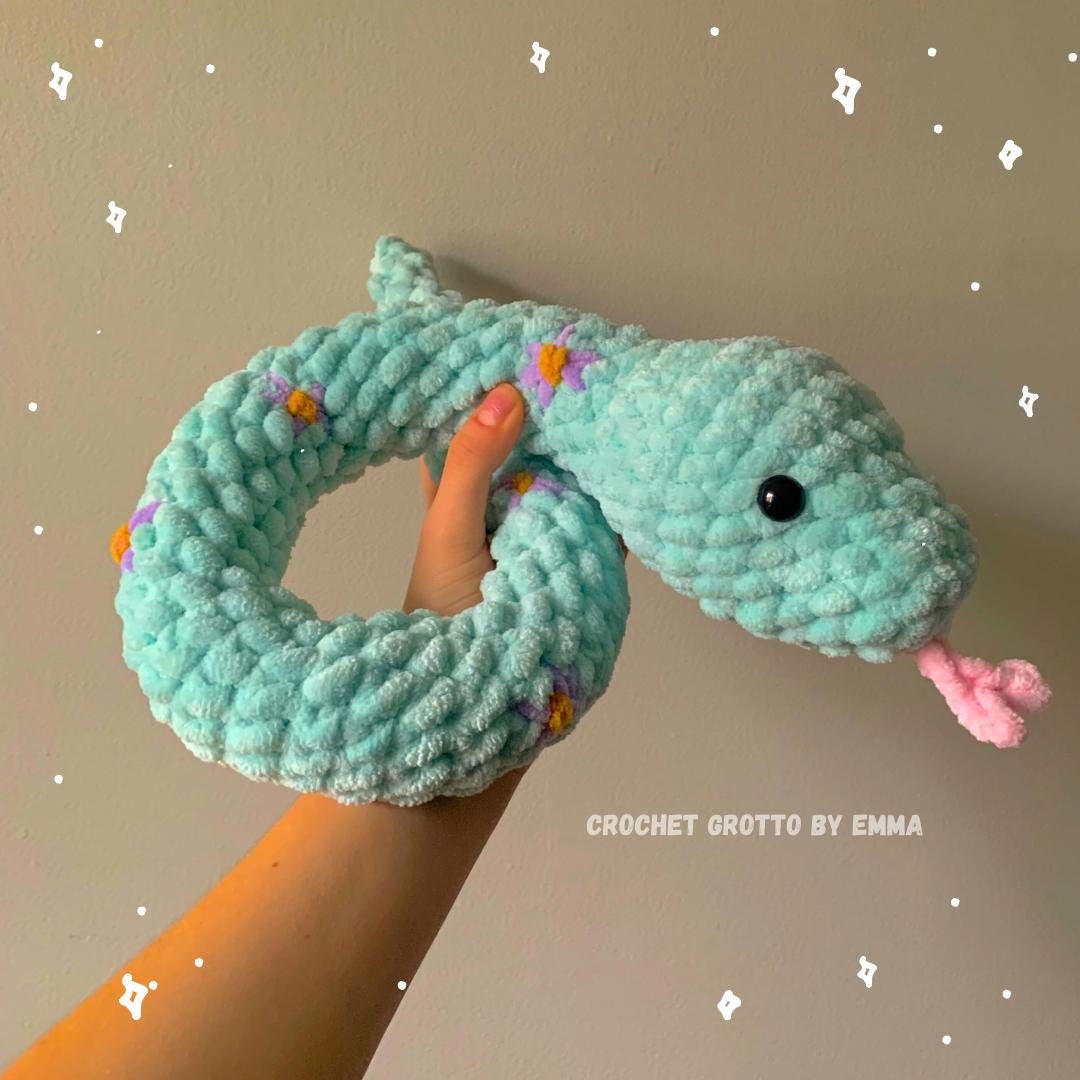 A turquoise, fluffy crochet snake plushie with embroidered flower details (in purple).